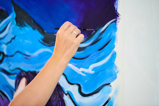 Woman artist hand holds paint brush and draws surreal fantasy image on white canvas at outdoor art painting festival, paintings art picture process. Woman artist paints atmospheric surreal picture - Fotoğraf, Görsel