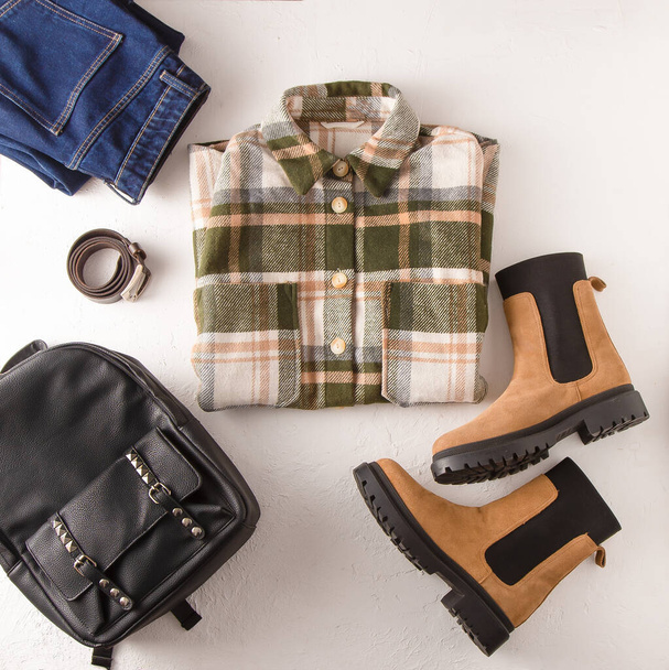 Set of clothes. Checked shirt, jeans, beige boots, leather backpack. Shoes and wardrobe. Womens modern style. Clothing top view. Woman clothes and accessories casual spring winter autumn outfit. - 写真・画像