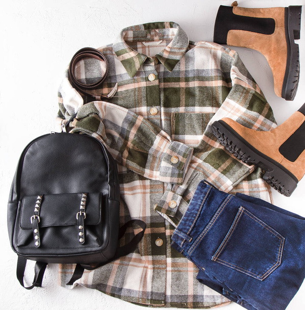 Set of clothes. Checked shirt, jeans, beige boots, leather backpack. Shoes and wardrobe. Womens modern style. Clothing top view. Woman clothes and accessories casual spring winter autumn outfit. - 写真・画像
