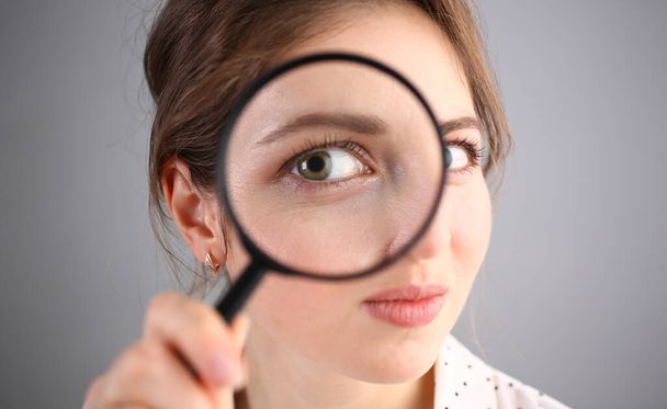Inquisitive young woman looking through magnifying glass. Search for business ideas and new creative creative information - Photo, Image