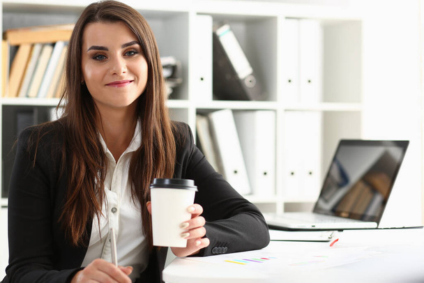 Beautiful young businesswoman holding glass of coffee at workplace. Break and rest in office concept - Foto, afbeelding