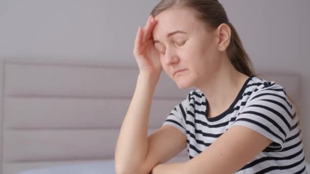 Atrakcyjna młoda kobieta siedzi na kanapie w swoim salonie w domu, czując ból głowy, zmęczony i zmartwiony, i cierpi na depresję. - Materiał filmowy, wideo
