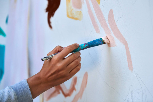 La mano del artista sostiene el pincel de pintura y dibuja una imagen surrealista abstracta sobre lienzo blanco en el festival de pintura de arte al aire libre, el proceso de pintura. Artista pinta cuadro atmosférico - Foto, Imagen