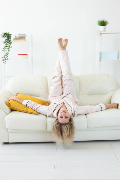 Smiling blonde woman sitting on comfortable coach in living room in pajama - homewear and free time holidays at home - Foto, Imagem