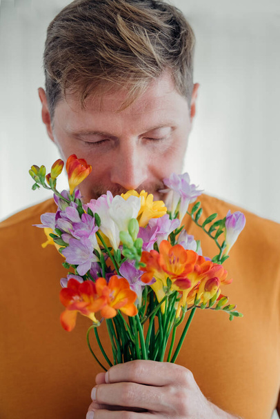 Front view man inhales aroma of cute bouquet of spring flowers. Selective focus - Foto, afbeelding