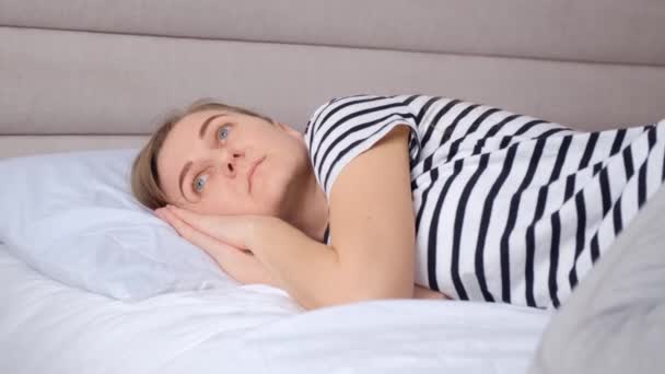 Europejka leżąca w łóżku z powodu zmęczenia pracą cierpi na bezsenność. Kobieta jest zmęczona, przygnębiona.. - Materiał filmowy, wideo