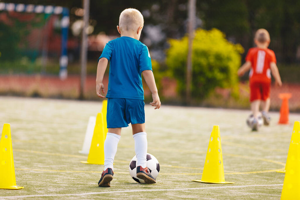 School children having fun at soccer training. Little blonde boy kicking a soccer ball at practice session dribbling drill between yellow cones. Soccer training dribbling drill for youth.  - Foto, Imagen