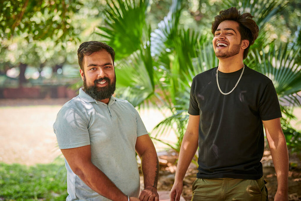 Zwei lustige indische Männer lachen und sprechen Hindi im öffentlichen Park grüne Palmenblätter Hintergrund, echte Männerfreundschaft. Zwei amüsante indische Jungs lachen laut über Outdoor-Spaziergänge im Park - Foto, Bild