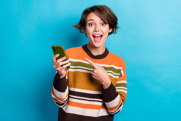 Photo of impressed woman with short hairstyle striped jumper directing at phone unbelievable unexpected isolated on blue color background. - Fotografie, Obrázek