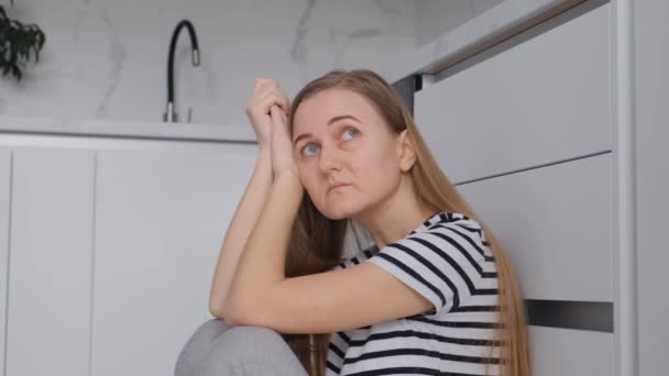Avrupa görünümlü yorgun bir kadın mutfakta yerde oturur ve dinlenir. Depresyon ve umutsuzluk içindeki bir kadın - Video, Çekim