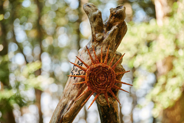 Symbol Amber Sun na pniu drzewa na zielonym tle lasu, obiekt sztuki dekoracyjnej z małych bursztynowych kamieni na wystawie sztuki plenerowej w parku publicznym. Piękna ozdoba rzemiosła bursztynowego słońca - Zdjęcie, obraz