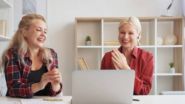 Fun webinar. Online interview. Virtual communication. Joyful women enjoying watching video on computer laughing at home office interior. - Fotografie, Obrázek