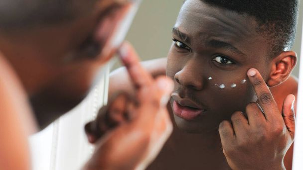 Facial cream. Skin treatment. Anti-aging skincare. Closeup of man applying under eye face moisturizing cosmetic product in mirror reflection. - Foto, afbeelding