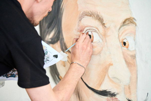 Young man artist draws with paint brush surreal man portrait on white canvas at art painting festival, paintings art picture process. Woman paints Salvador Dali portrait, art of atmospheric surrealism - Photo, image