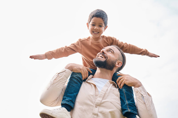 Family, kids and boy sitting on the shoulders of his father outdoor while bonding from below. Fun, children and love with a man carrying his son outside while spending time together being playful. - Photo, image