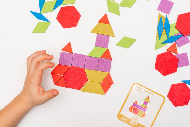 Close up of kid hands playing bright wooden tangram toy. The child collects a pattern of wooden bars. Creative baby make new forms. - Foto, Imagem