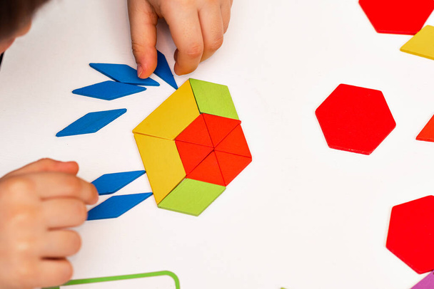 Close up of kid hands playing bright wooden tangram toy. The child collects a pattern of wooden bars. Creative baby make new forms. - Fotó, kép