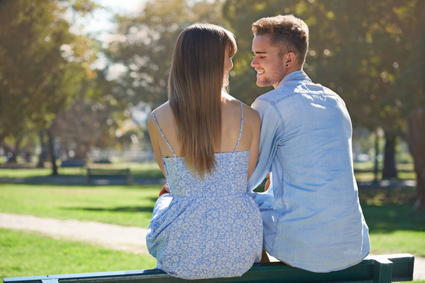Ηλιόλουστη μέρα αγάπης. Στιγμιότυπο ενός νεαρού ζευγαριού που κάθεται σε ένα παγκάκι και απολαμβάνει μια μέρα στο πάρκο. - Φωτογραφία, εικόνα