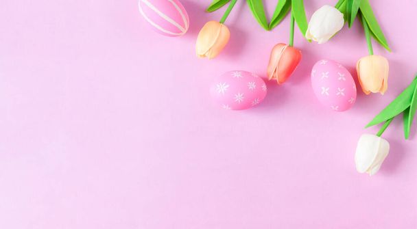 Happy Easter holiday greeting card concept. Colorful Easter Eggs and spring flowers on pastel pink background. Top view, flat lay, copy space. - Fotó, kép