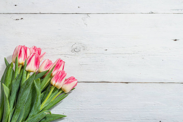 Kytice čerstvých růžových tulipánů na bílém dřevěném pozadí. Slavnostní koncept na Den matek nebo na Valentýna. Pozdrav, Velikonoční byt ležel, tvrdé světlo, tmavý stín, horní pohled - Fotografie, Obrázek