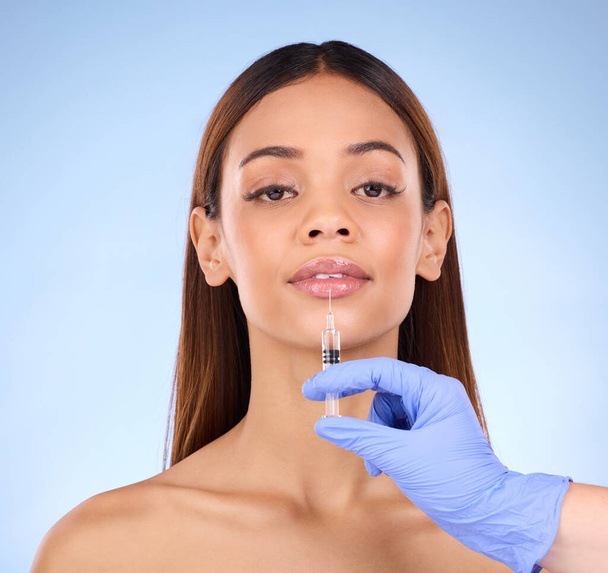 Portrait, lips and injection of woman on studio, blue background and facial beauty. Young female model, lip filler and needle for plastic surgery, skincare transformation and aesthetic face change. - Foto, imagen