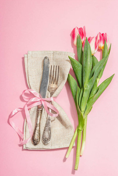 Romantic table setting with pink tulips. Vintage cutlery, fresh flowers, linen napkin. Festive concept background, flat lay, hard light, dark shadow, top view - Photo, Image
