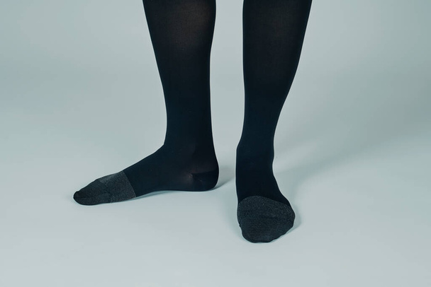 close-up das pernas de um pé sobre um homem de fundo esbranquiçado vestindo um par de meias de compressão preta - Foto, Imagem