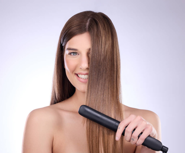 Hair straightener, face portrait and beauty of woman in studio isolated on a gray background. Haircare, happy and female model with flat iron product for salon treatment, balayage and hairstyle - Photo, Image