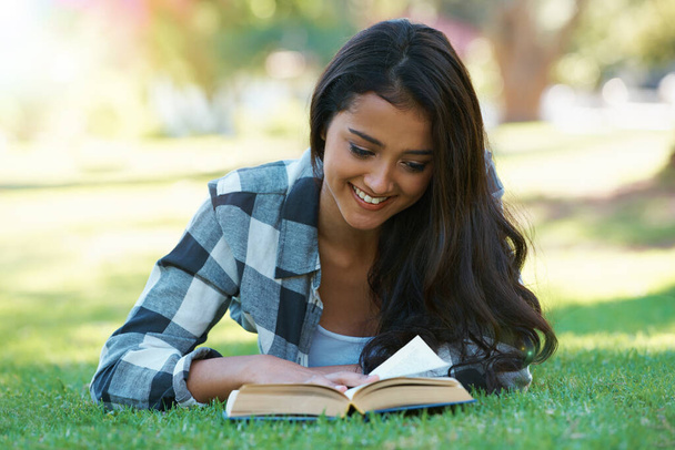 Se détendre avec un bon livre. une jeune femme allongée sur l'herbe et lisant un livre - Photo, image