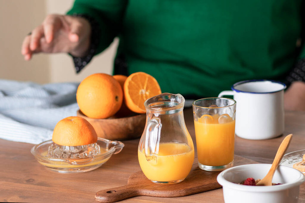 Bodegón de jugo de naranja y cereales. Fondo desenfoque una persona exprimiendo naranjas en un exprimidor. - Foto, Imagen