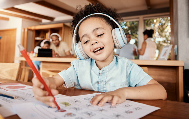 Distance learning, headphones and student doing homework while listening to music, audio book or radio. Home school, education of young kid or boy child writing on paper for academic or project. - Foto, imagen
