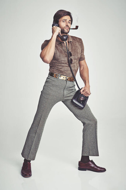 Doing everything with flair. A handsome man on a retro telephone while striking a pose - Foto, imagen