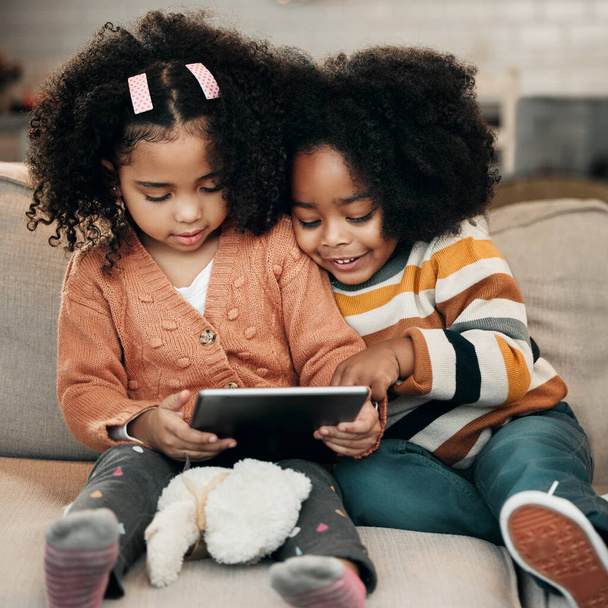 Szczęśliwe dzieci na sofie z tabletem do edukacji online, zabawy gry i oglądać kreskówki internetowej lub wideo razem. Dzieci z rodziny birasowej na kanapie z cyfrową technologią, aplikacją lub internetem do streamingu filmów. - Zdjęcie, obraz
