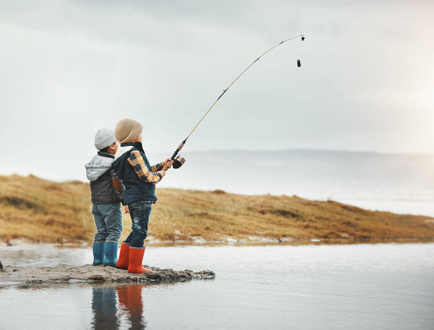 Lake, activity and children fishing while on vacation, adventure or weekend trip for a hobby. Outdoor, nature and boy siblings or kids catching fish in water together while on holiday in countryside - Фото, изображение