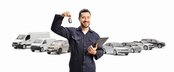 Auto mechanic holding car key in front of different parked vehicles isolated on white background - Foto, Bild