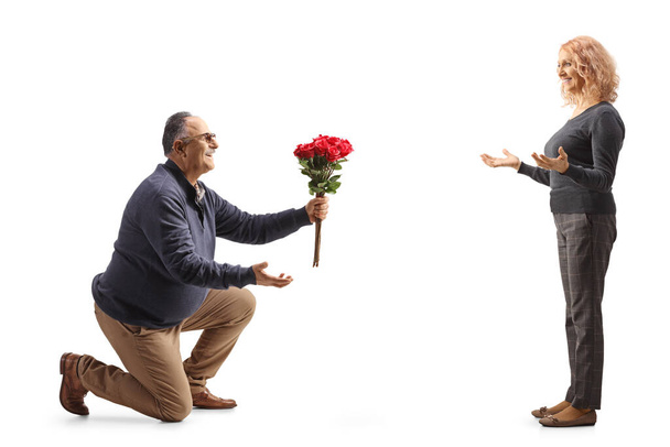 Mature man kneeling and giving a bunch of red roses to a woman isolated on white background - Foto, imagen
