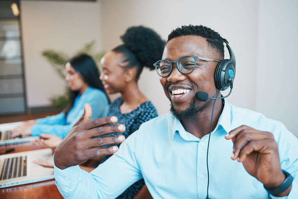 An attractive Black man speaks to client on headset remote call, smiling. High quality photo - Φωτογραφία, εικόνα