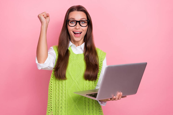 Photo of young overjoyed positive brunette hair business lady wear green classic vest fist up hold netbook victory isolated on pink color background. - 写真・画像