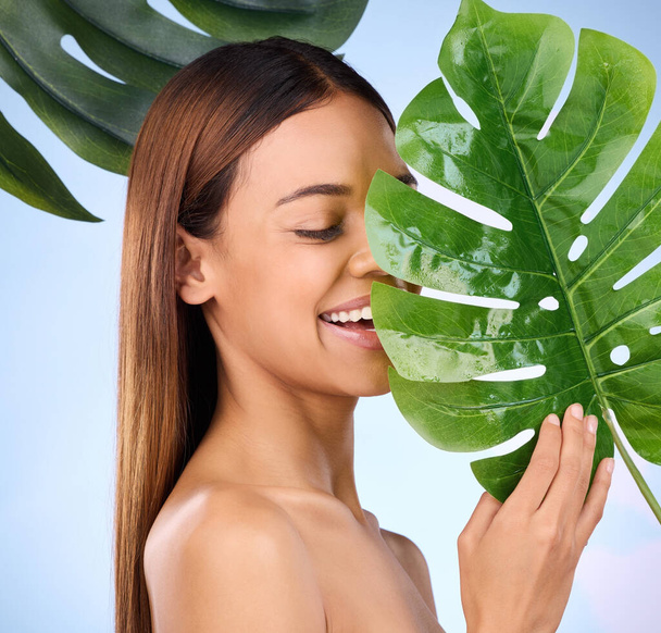 Woman, smile and leaf in natural beauty and organic skincare cosmetics for self love or care against a blue studio background. Happy female smiling and holding leafy green plant for healthy wellness. - Fotoğraf, Görsel