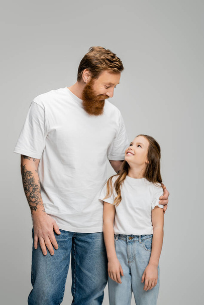 Tattooed father hugging preteen daughter isolated on grey  - Foto, imagen