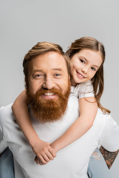 Overjoyed preteen girl piggybacking on bearded dad isolated on grey - Photo, Image