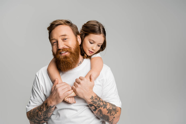 Preteen κορίτσι αγκαλιάζει τατουάζ και χαρούμενος πατέρας απομονώνονται σε γκρι  - Φωτογραφία, εικόνα