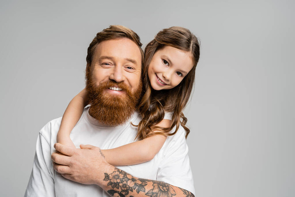 Positive girl hugging tattooed father in t-shirt isolated on grey  - Фото, зображення