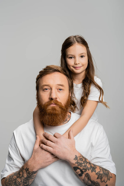 Mosolygó lány ölelés tetovált apa fehér pólóban elszigetelt szürke  - Fotó, kép