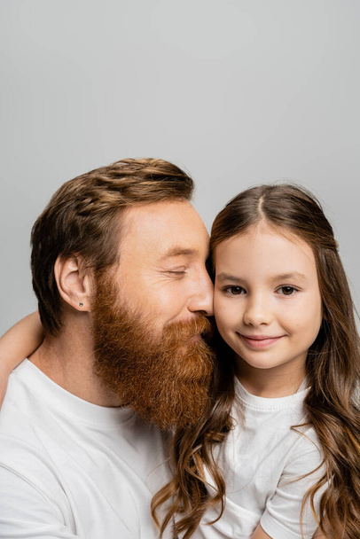Smiling girl hugging bearded father and looking at camera isolated on grey  - 写真・画像