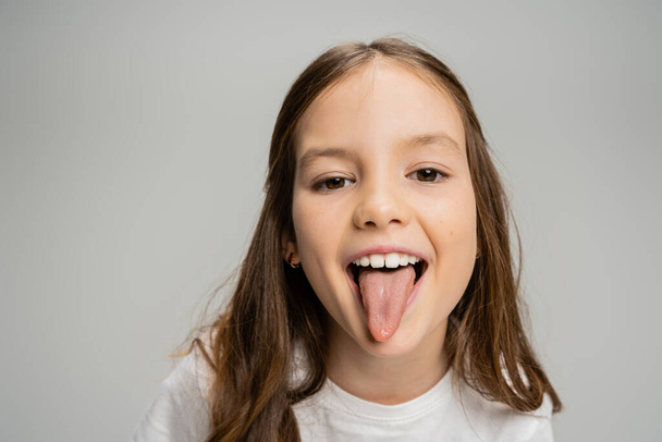 Preteen kid sticking out tongue at camera isolated on grey   - Photo, Image