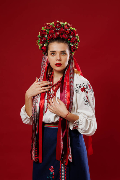 Portrait of ukrainian woman in traditional ethnic clothing and floral red wreath on viva magenta studio background. Ukrainian national embroidered dress call vyshyvanka. Pray for Ukraine - Photo, Image