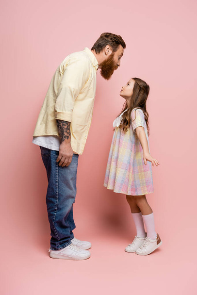 Zijaanzicht van vader en dochter pruilen lippen op roze achtergrond  - Foto, afbeelding
