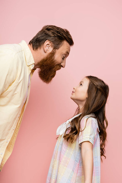 Vista lateral de pai alegre e filha pré-adolescente de pé isolado em rosa   - Foto, Imagem