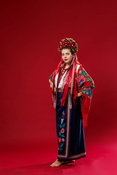 Portrait of ukrainian woman in traditional ethnic clothing and floral red wreath on viva magenta studio background. Ukrainian national embroidered dress call vyshyvanka. Pray for Ukraine - Fotoğraf, Görsel